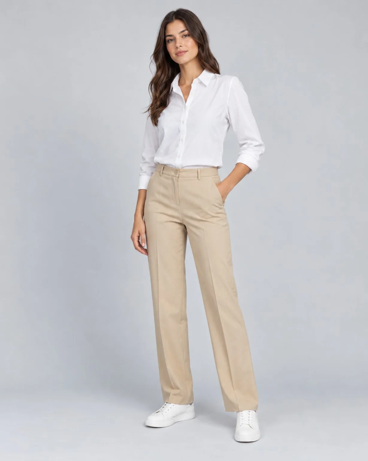 Modelo con camisa blanca, pantalón beige y zapatillas sobre un fondo claro de estudio